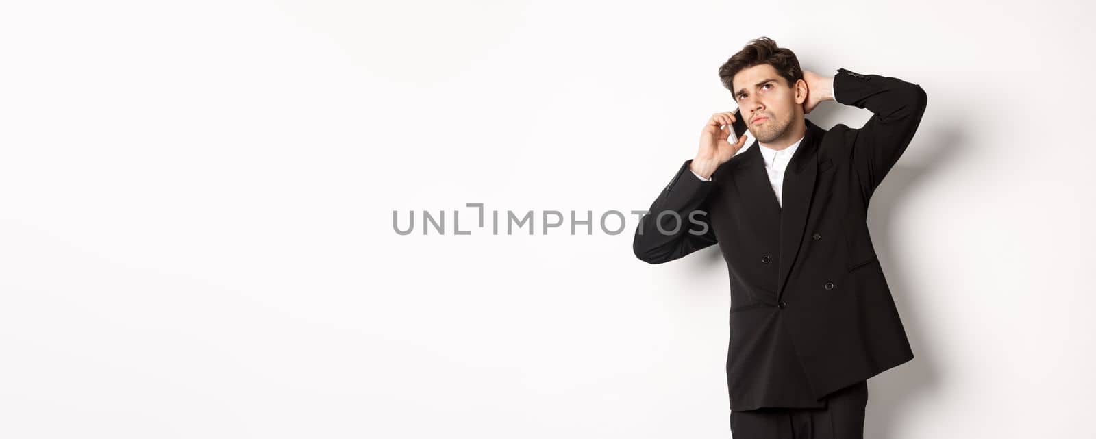 Image of indecisive businessman talking on phone and thinking, looking doubtful, making decision, standing over white background by Benzoix