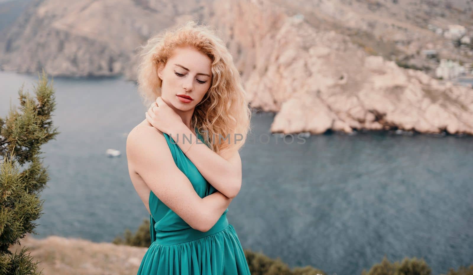 Redhead woman portrait. Curly redhead young caucasian woman with freckles looking at camera and smiling. Close up portrait cute woman in a mint long dress posing on a volcanic rock high above the sea by panophotograph