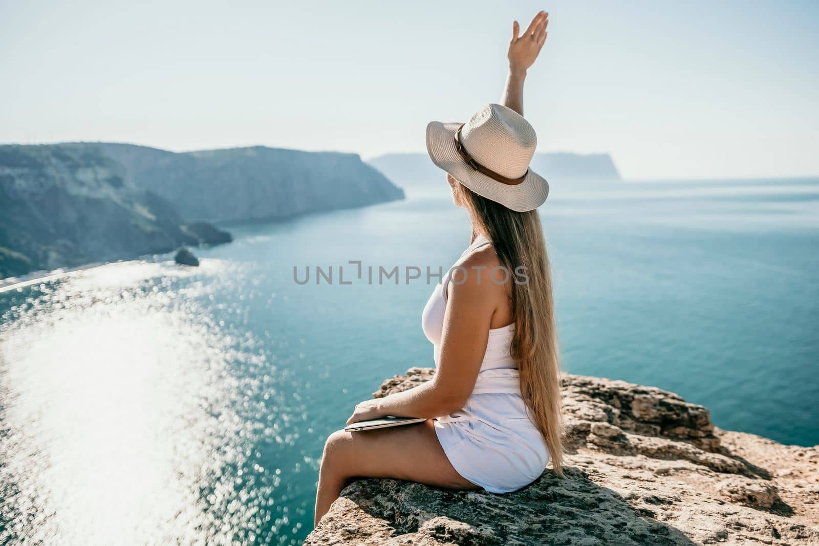 Successful business woman in yellow hat working on laptop by the sea. Pretty lady typing on computer at summer day outdoors. Freelance, travel and holidays concept.