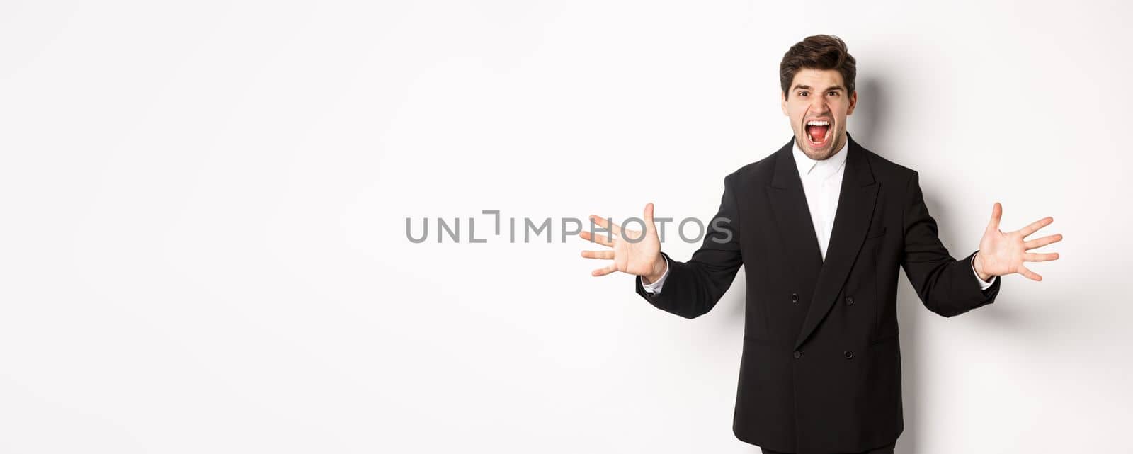 Portrait of pissed-off and frustrated businessman in suit, shouting angry and shaking hands, standing distressed against white background.