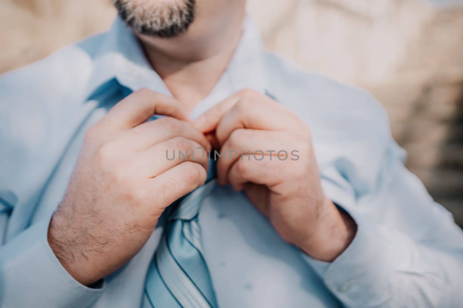 Close up of Man Adjusting Tie of Suit. Businessman in blue shirt straightens his tie, close-up by panophotograph