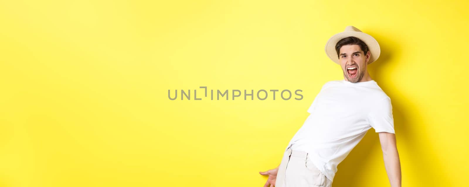 Concept of tourism and vacation. Excited young man tourist celebrating, shouting for joy and dancing, standing over yellow background.