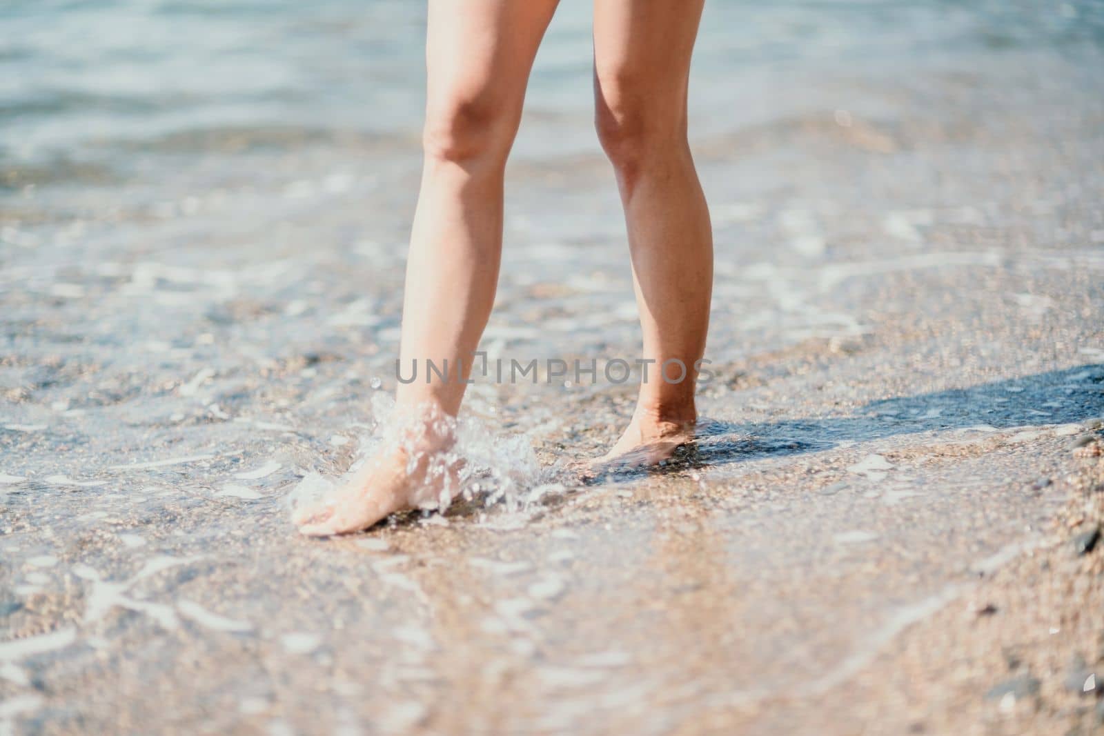 Barefoot woman standing in sea, summer vacation on beach resort. Naked female legs in transparent calm water