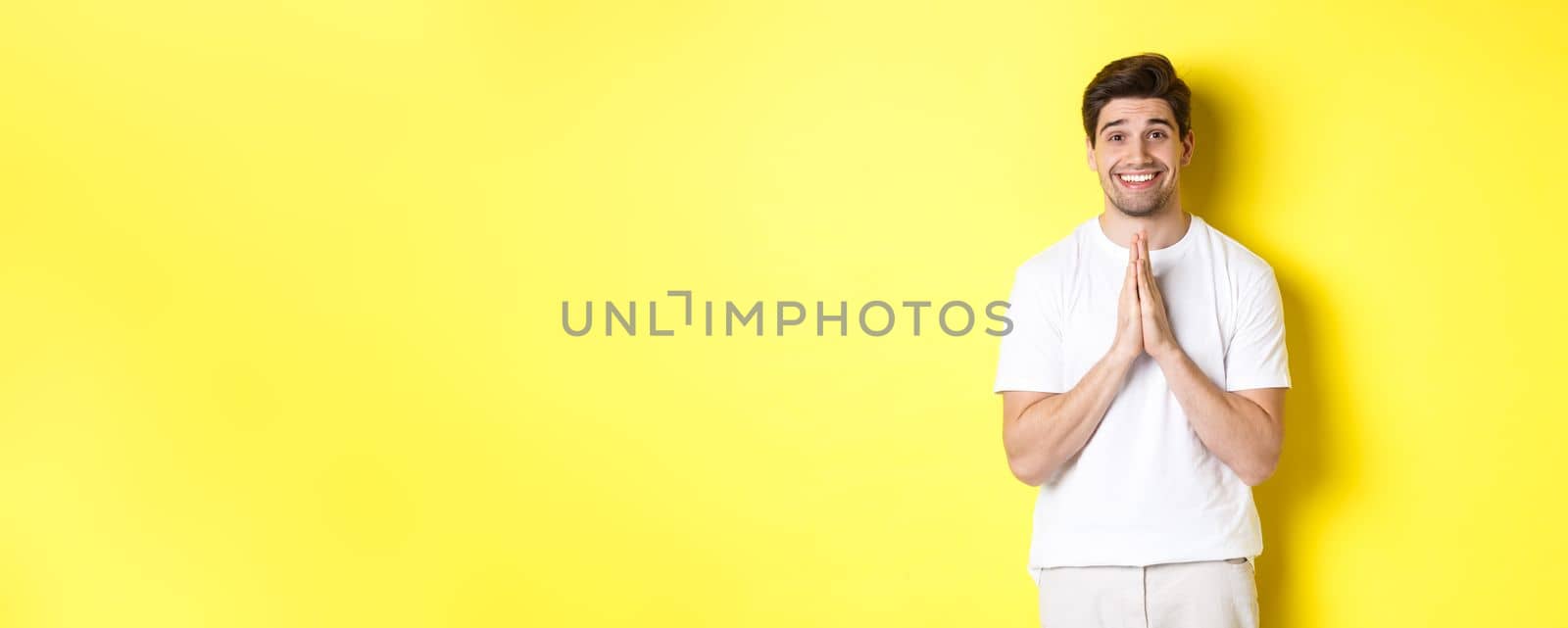 Hopeful man asking for help, begging favour, need something and smiling, standing over yellow background.