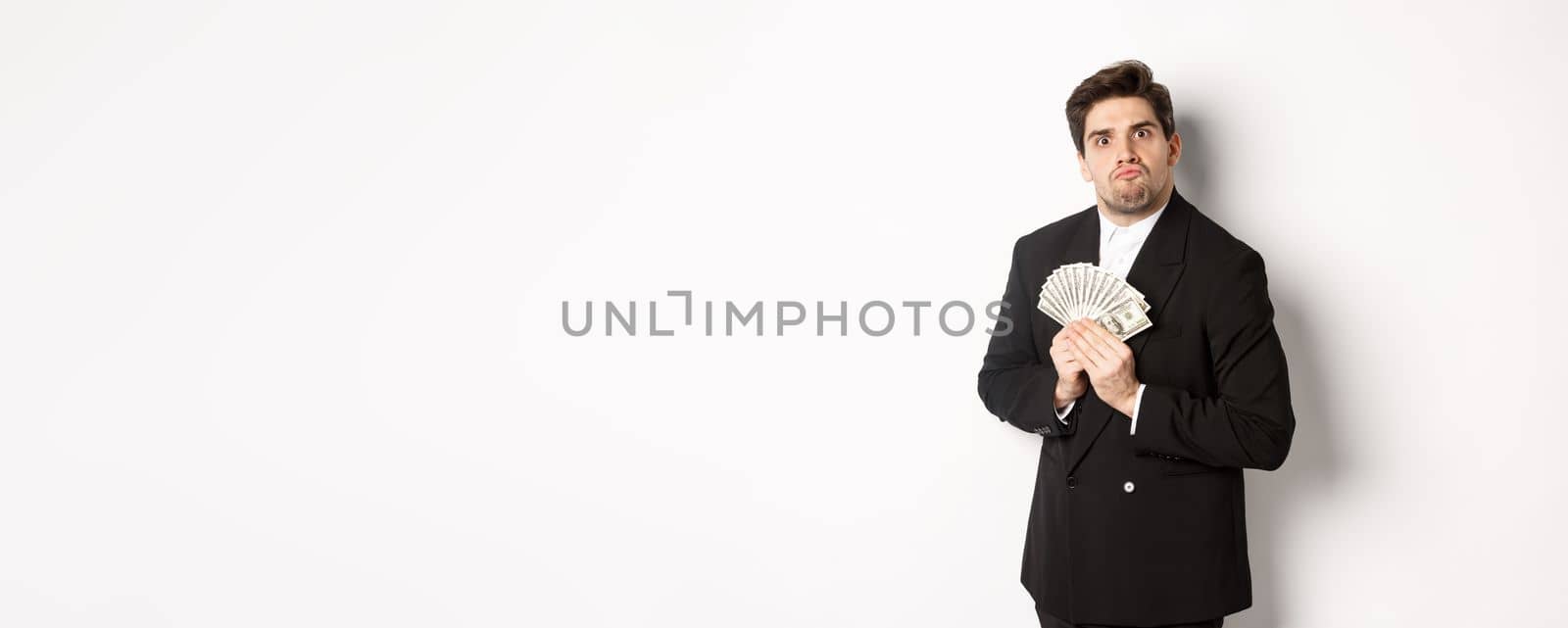 Image of greedy guy in black suit, holding money and unwilling to share, standing over white background by Benzoix