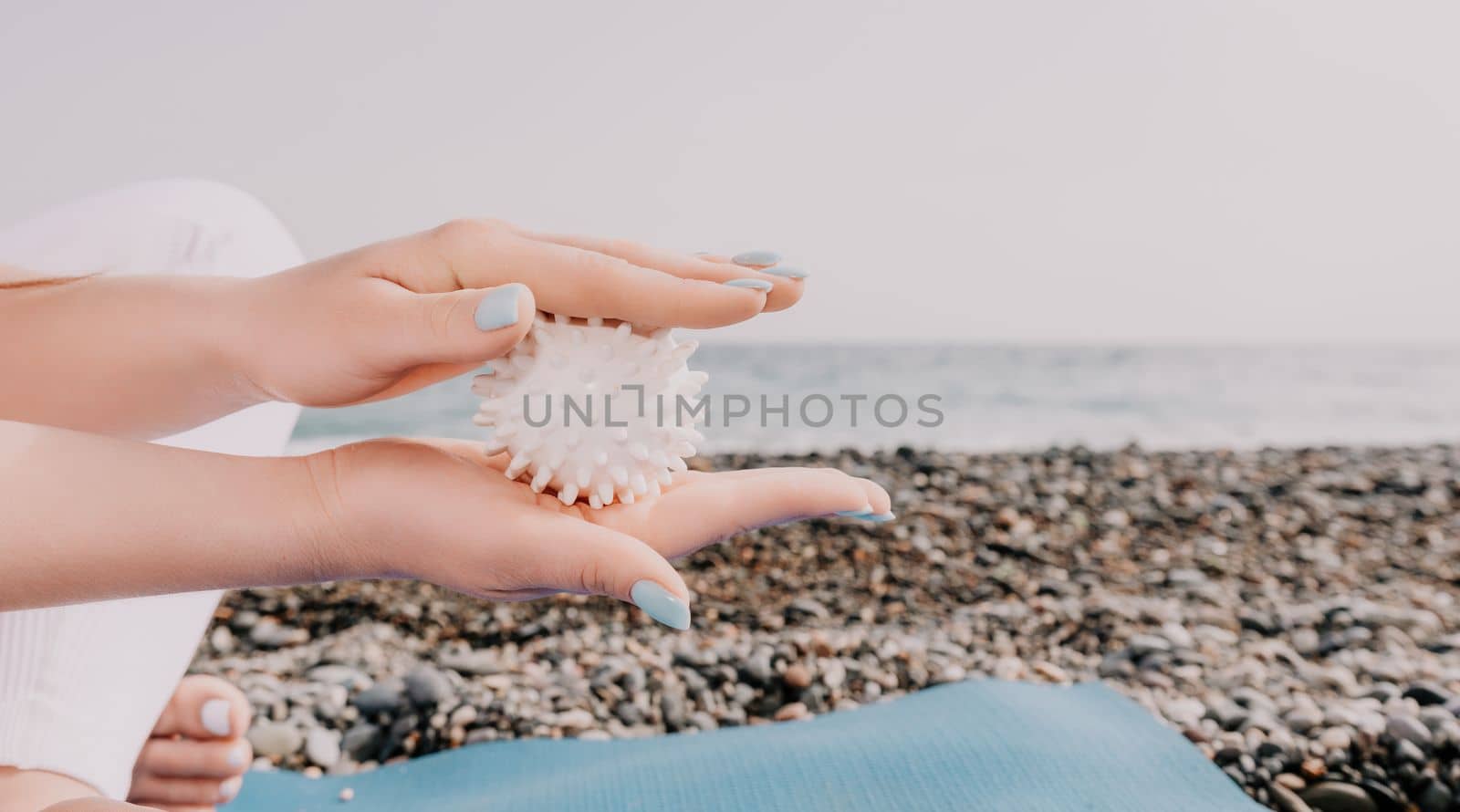 Woman yoga sea. Well looking middle aged woman with braids dreadlocks in white leggings and tops doing stretching pilates on yoga mat near sea. Female fitness yoga routine concept. Healthy lifestyle