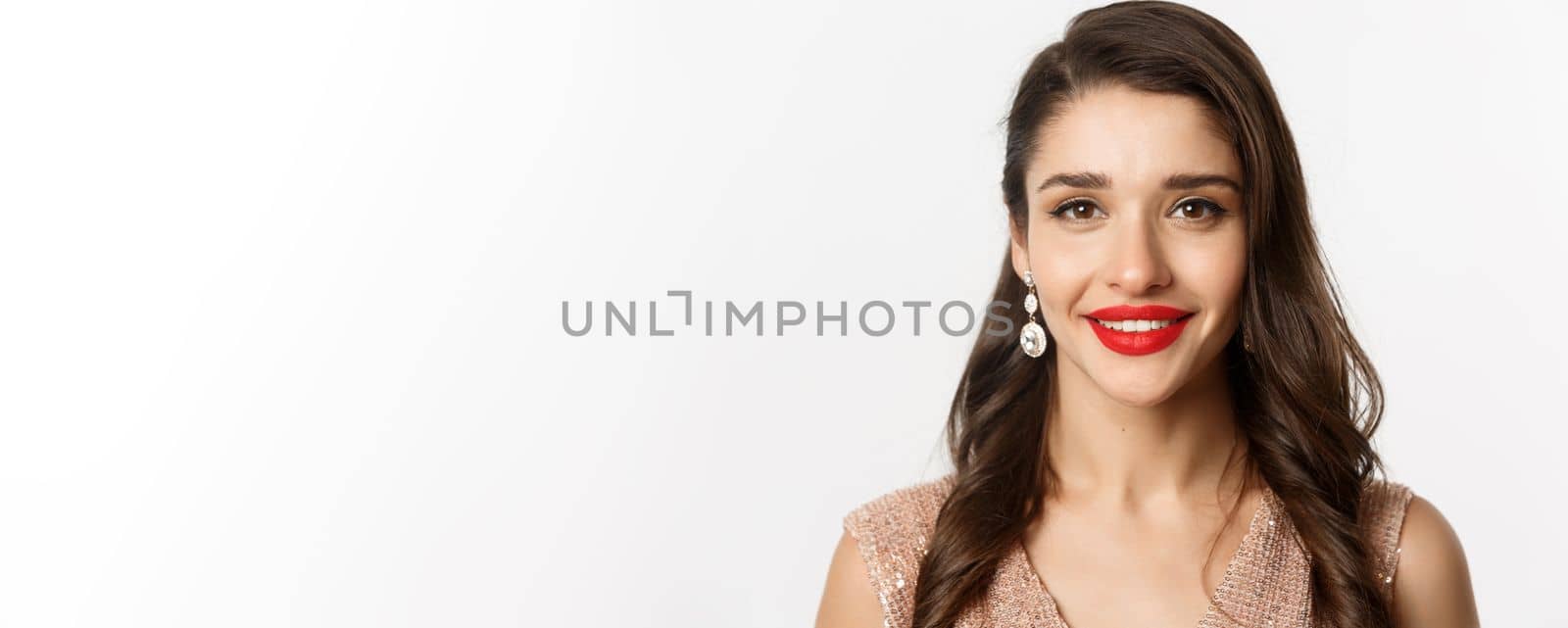 Concept of New Year celebration and winter holidays. Headshot of beautiful young woman with red lips, wearing luxury earrings, smiling happy at camera, white background by Benzoix