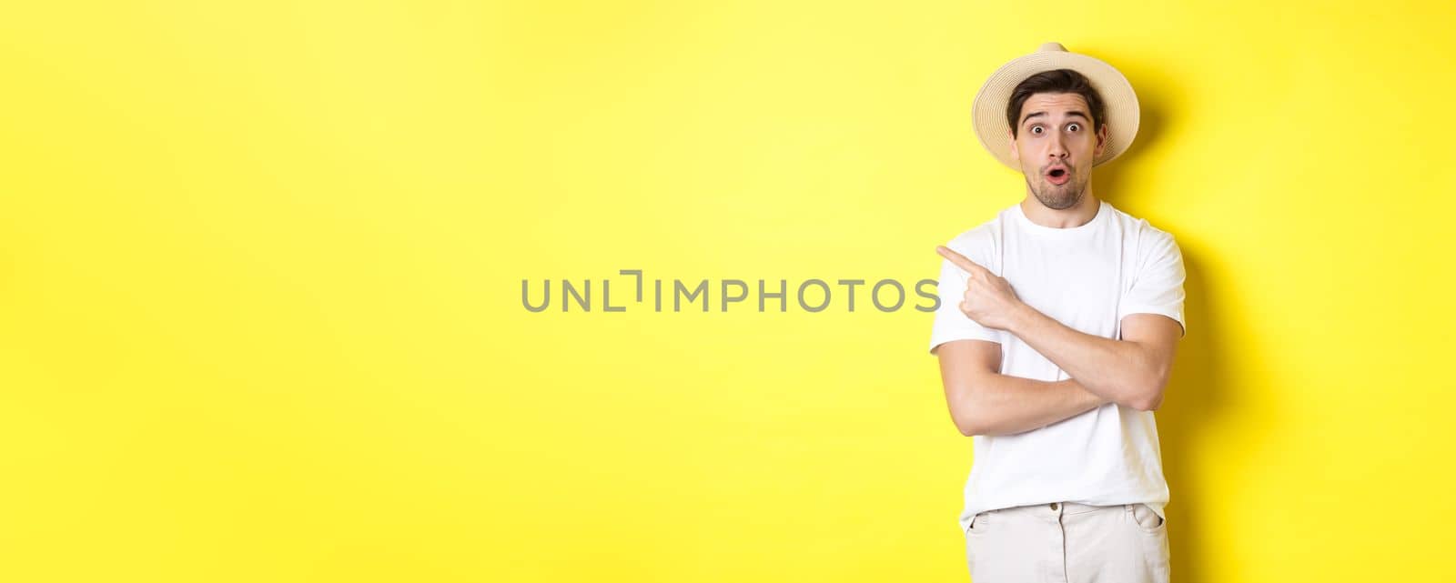 Concept of tourism and lifestyle. Surprised handsome man tourist pointing finger left, looking impressed about promo offer, yellow background by Benzoix