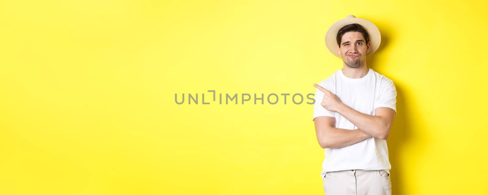 Concept of tourism and lifestyle. Skeptical guy tourist complaining, pointing finger left at something bad, looking displeased, yellow background by Benzoix