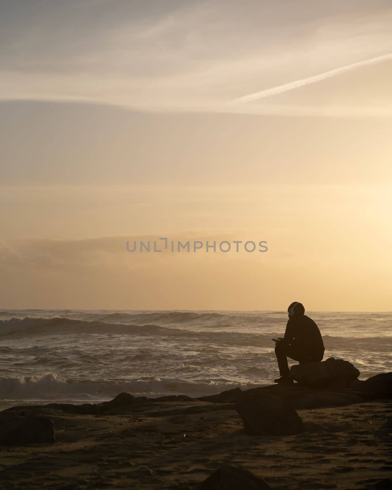 Silhouette of boy sitting with headphones on the seashore beach at sunset time. Handsome Asia man model in his 20s