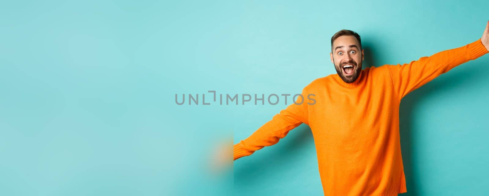 Surprised and happy man spread hands in warm welcome, reaching for hug, greeting you, showing something big, standing over light blue background.