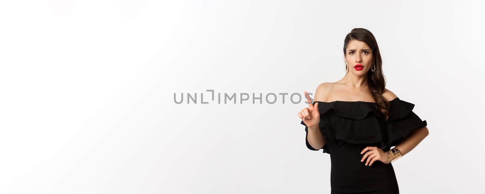 Fashion and beauty. Sassy woman in black dress saying no, disagree and shaking finger displeased, rejecting offer, declining something, standing over white background.