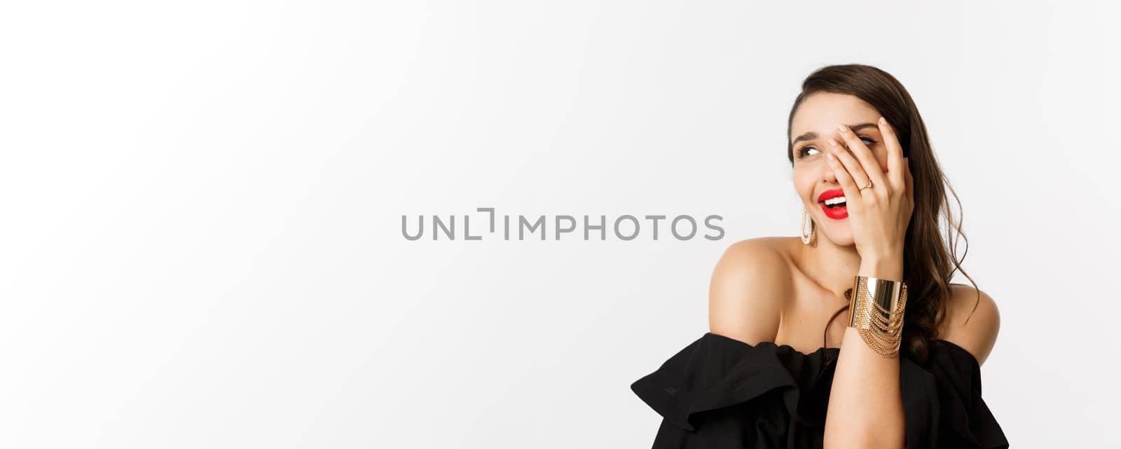 Close-up of beautiful woman show-off her engagement ring, showing hand and smiling coquettish, standing over white background by Benzoix