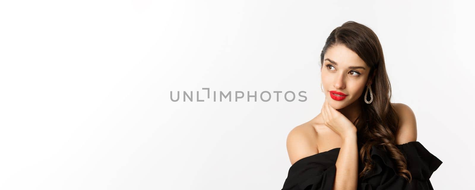 Fashion and beauty concept. Elegant woman with earrings and black dress, looking left sensual, standing over white background by Benzoix