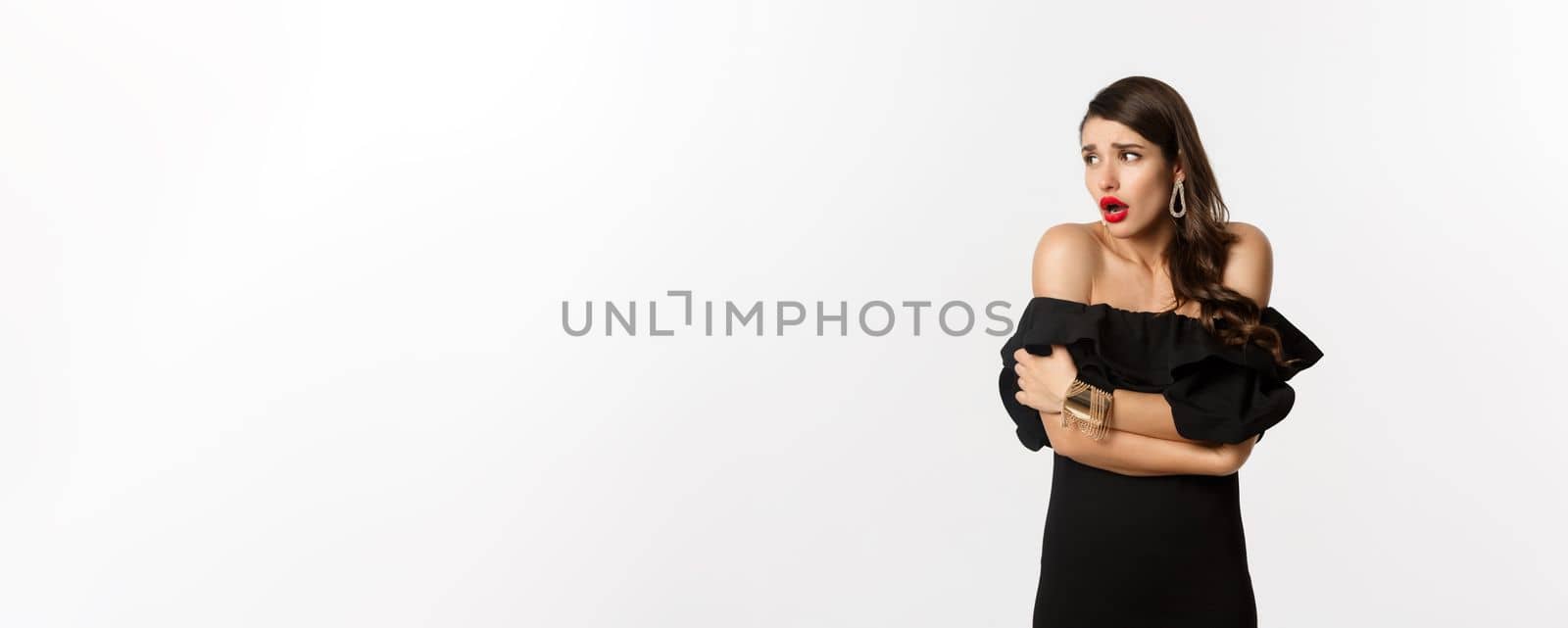 Image of scared and shocked glamour woman looking around, comfort herself, standing alarmed against white background.