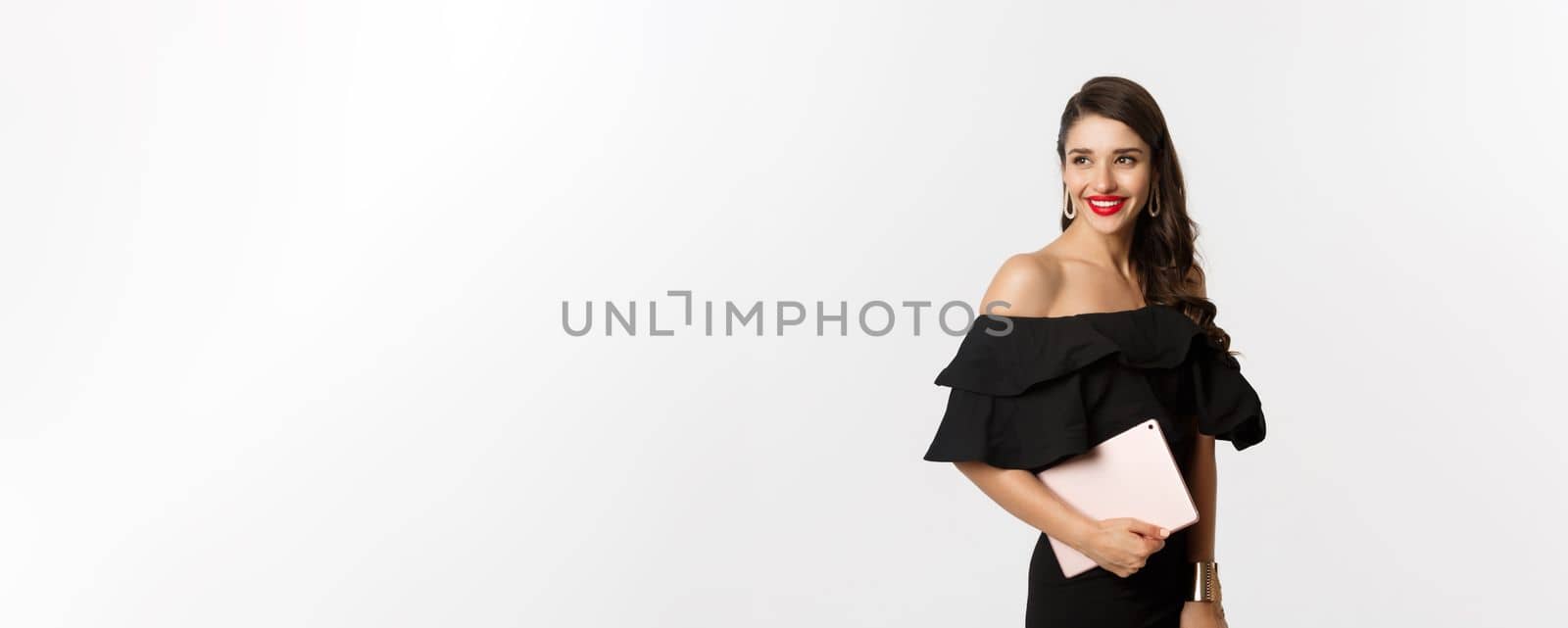 Fashion and shopping concept. Stylish young woman with glamour makeup, wearing black dress, holding digital tablet and smiling, white background by Benzoix