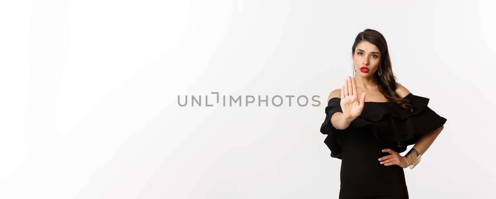 Fashion and beauty. Confident attractive woman telling no, showing stop gesture and looking serious at camera, disapprove and prohibit, standing over white background.