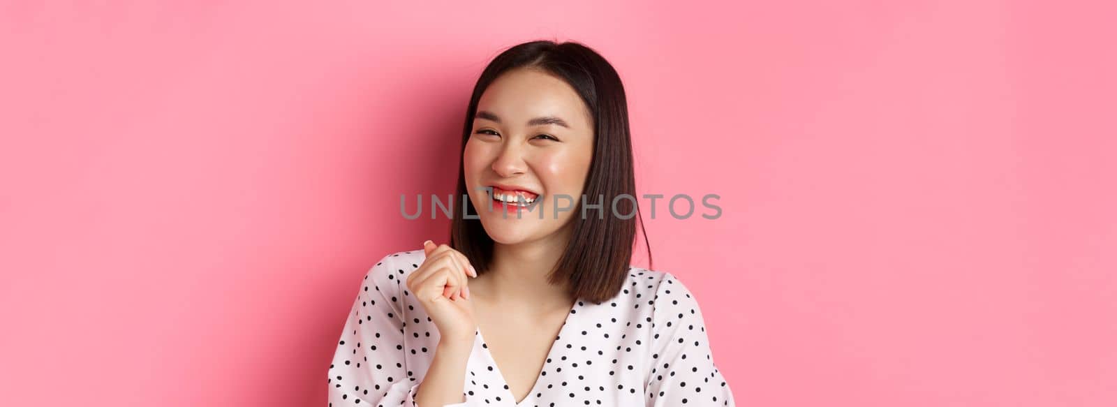 Beauty and lifestyle concept. Close-up of happy asian female laughing, looking happy and showing genuine emotions, standing over pink background by Benzoix