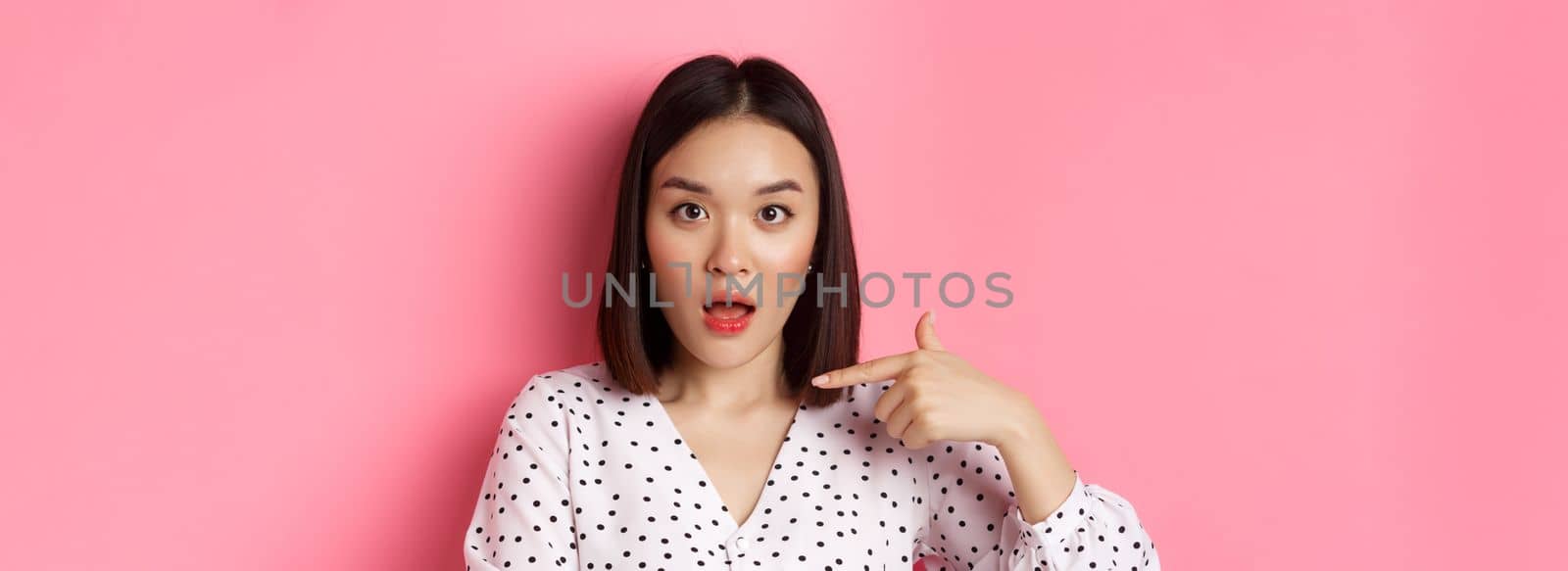Image of confused asian woman pointing at herself, drop jaw and staring questioned at camera, standing over pink background by Benzoix