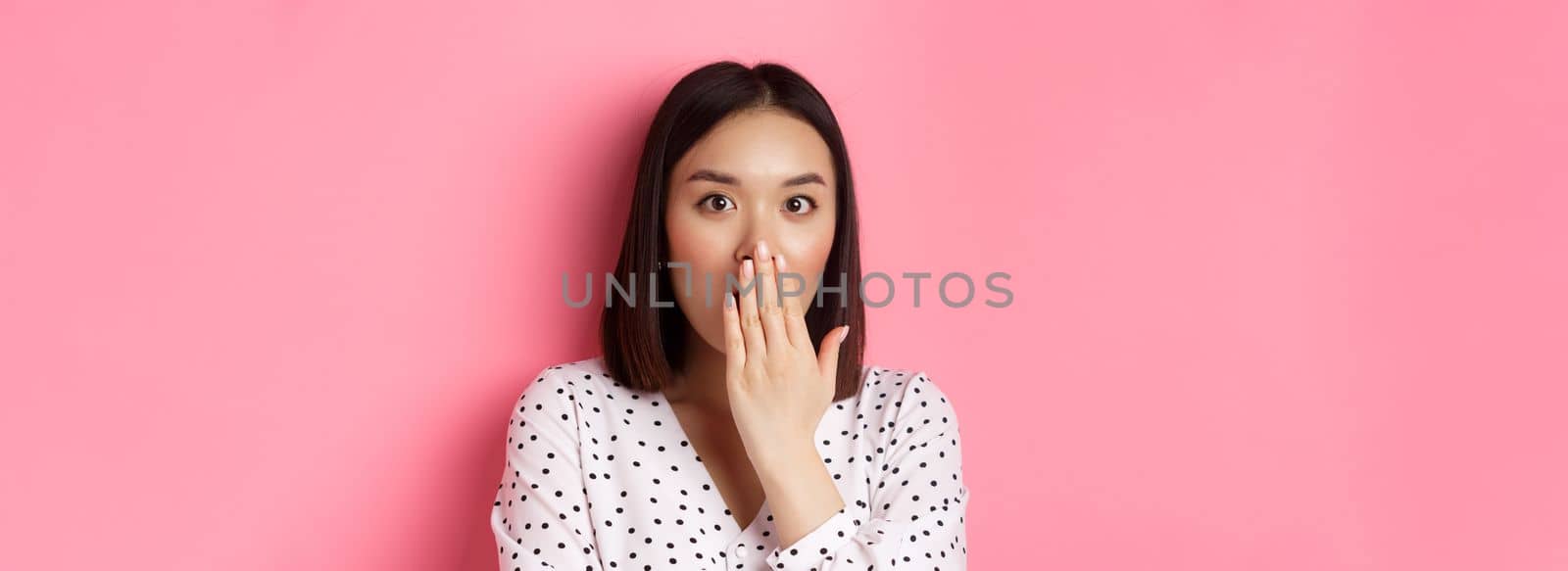Image of shocked asian girl gossiping, gasping and cover mouth, stare at camera with complete disbelief, standing over pink background by Benzoix