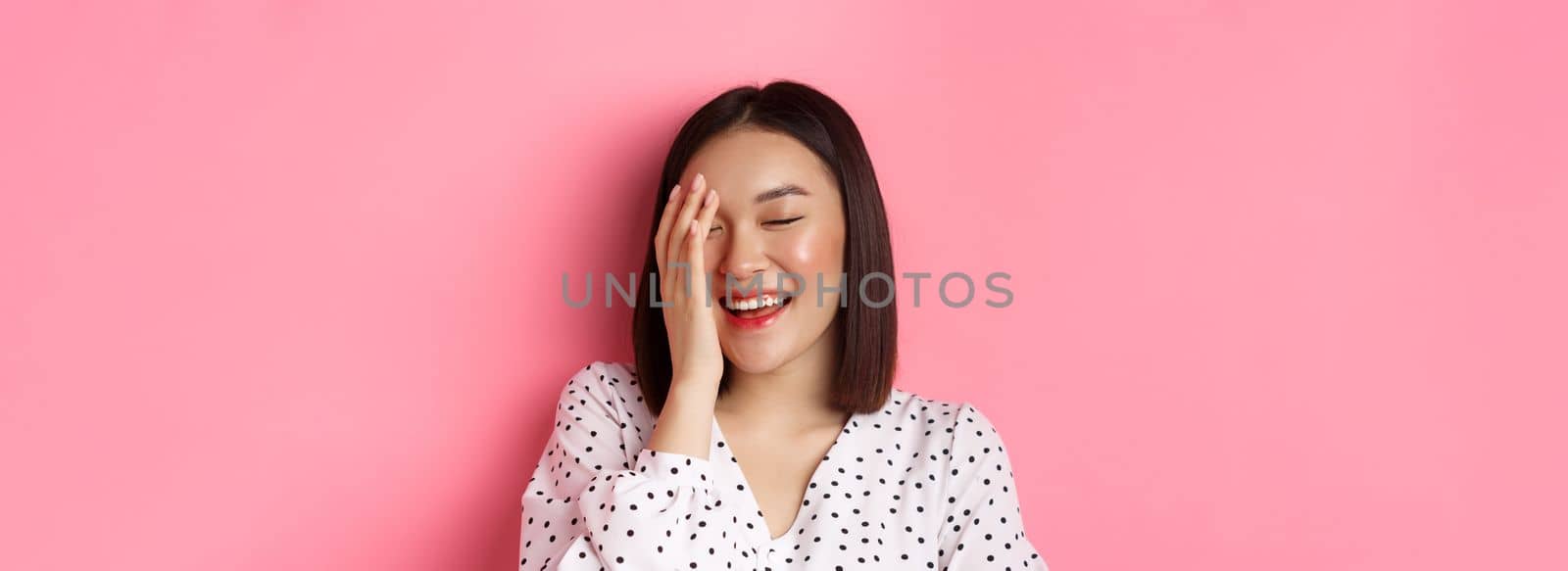 Beauty and lifestyle concept. Close-up of happy asian female laughing, looking happy and showing genuine emotions, standing over pink background by Benzoix