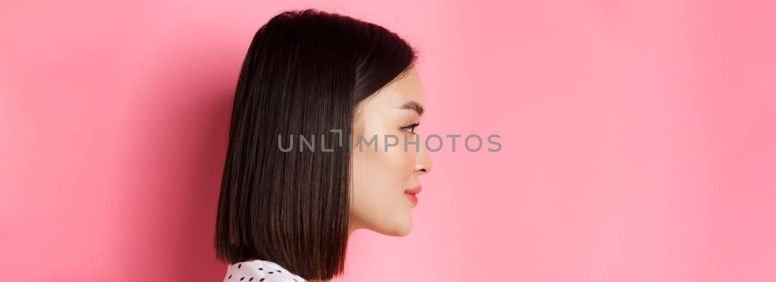 Beauty and skin care concept. Headshot profile of young beautiful asian woman with short dark hair, looking left at copy space, standing over pink background by Benzoix