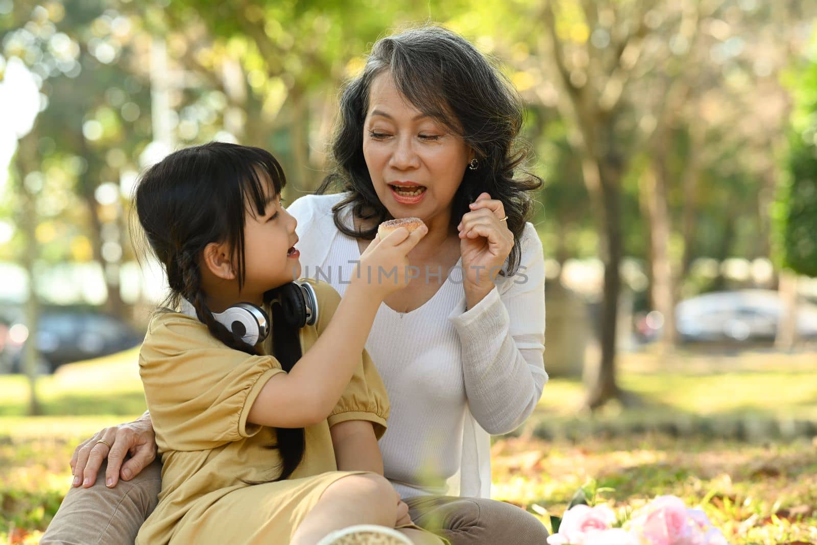 Happy middle aged woman and little granddaughter enjoying picnic in park together, spending leisure activity outdoor by prathanchorruangsak