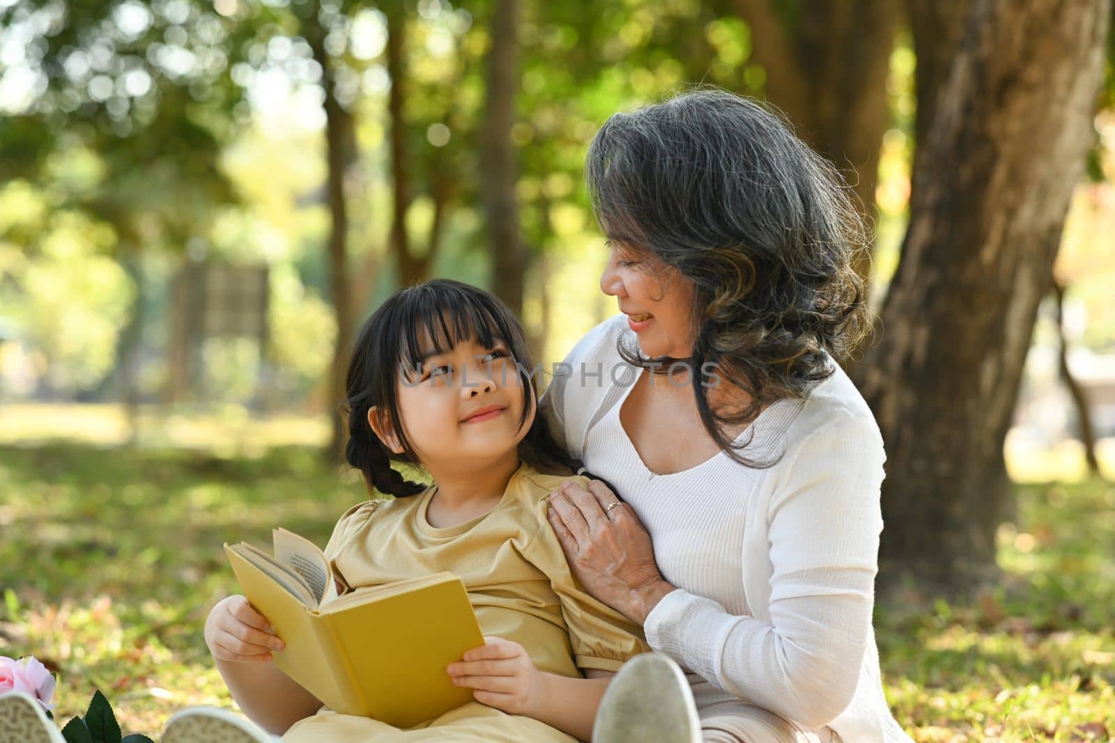 Loving mature grandma embracing and reading fairytale to little grandchild. Family, generation and people concept.