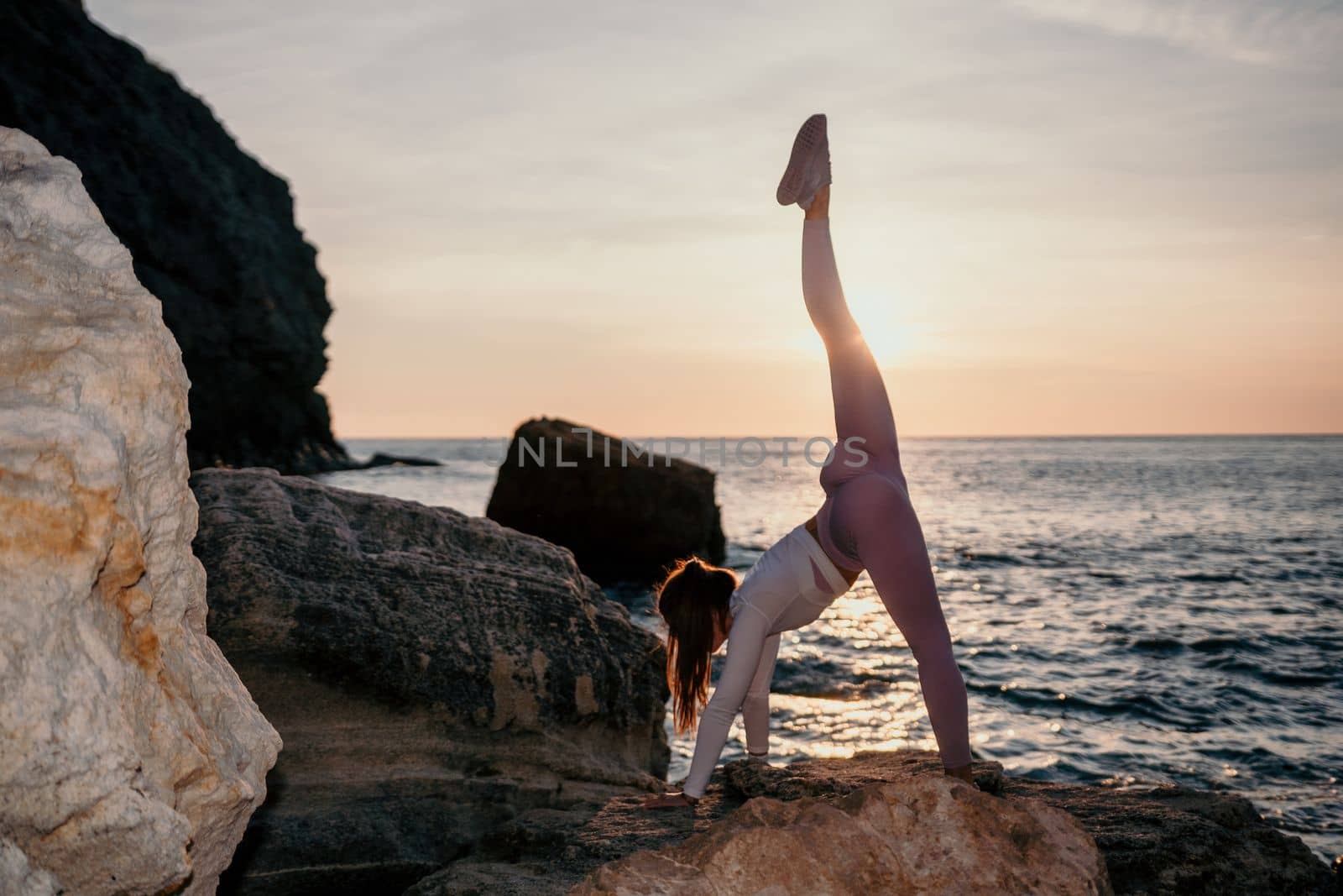 Young woman with black hair, fitness instructor in pink sports leggings and tops, doing pilates on yoga mat with magic pilates ring by the sea on the beach. Female fitness daily yoga concept