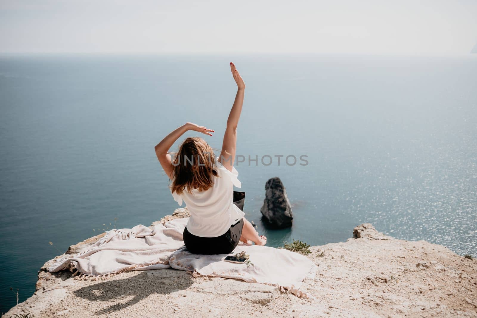 Successful business woman in yellow hat working on laptop by the sea. Pretty lady typing on computer at summer day outdoors. Freelance, travel and holidays concept.