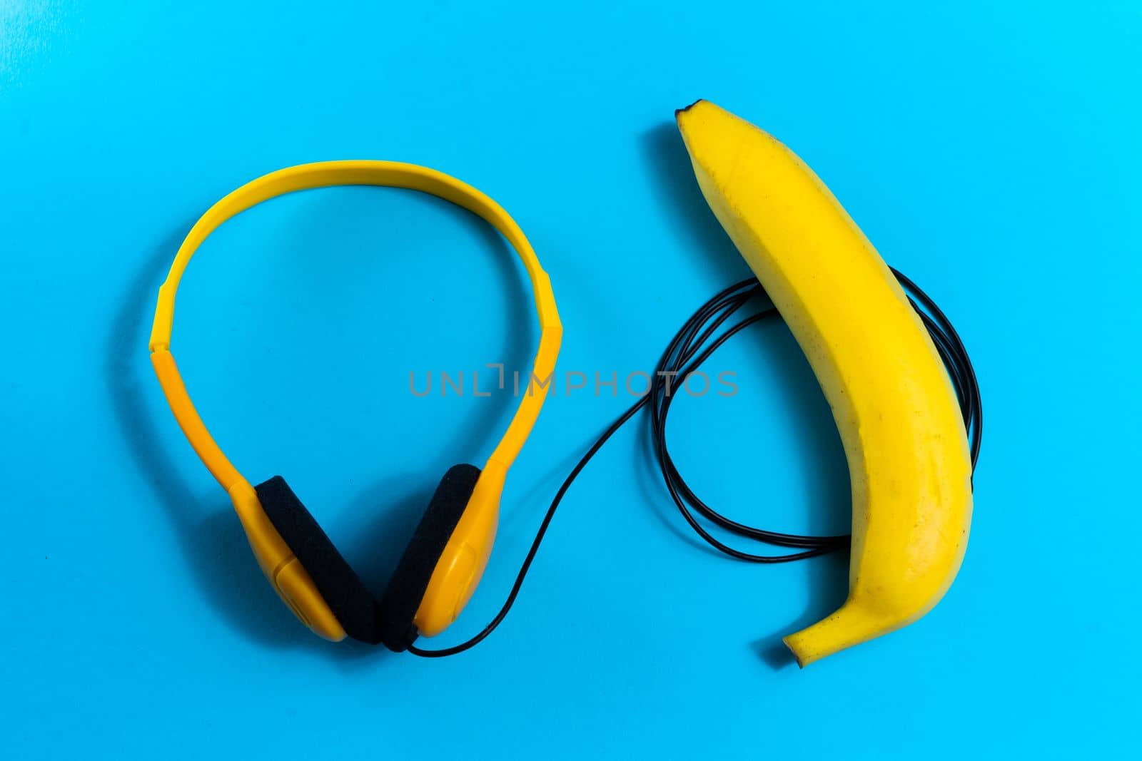Minimalism flat lay concept, listens to music. Headphones, banana on blue background. Top view by Zelenin