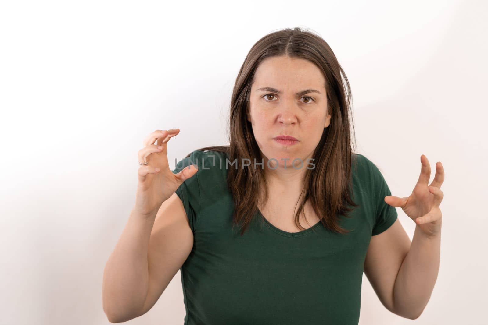 close-up of long-haired brunette woman looking at camera angry with open hands with angry gesture white background