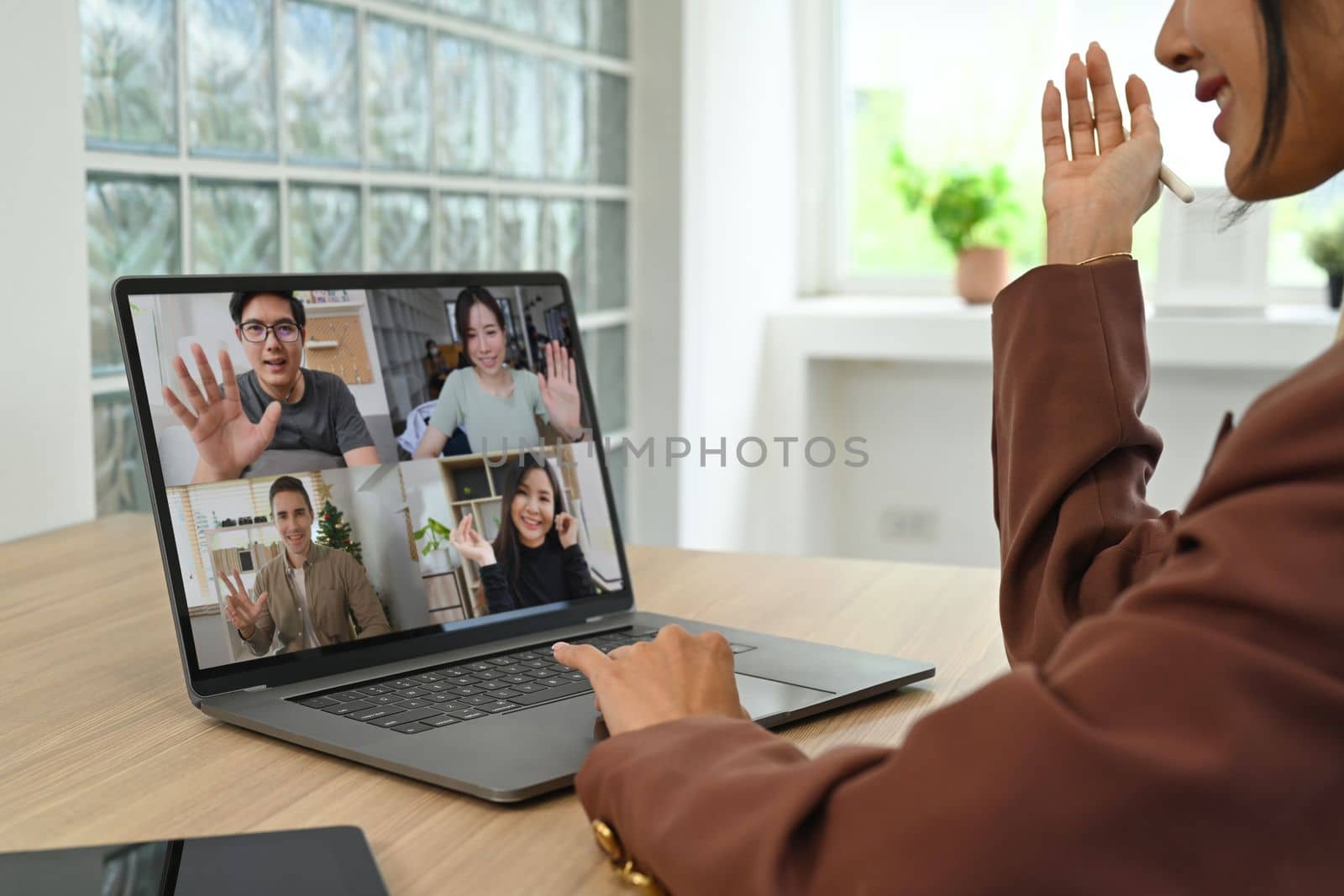 Smiling young female employee having video call with diverse colleagues on online briefing with laptop computer by prathanchorruangsak