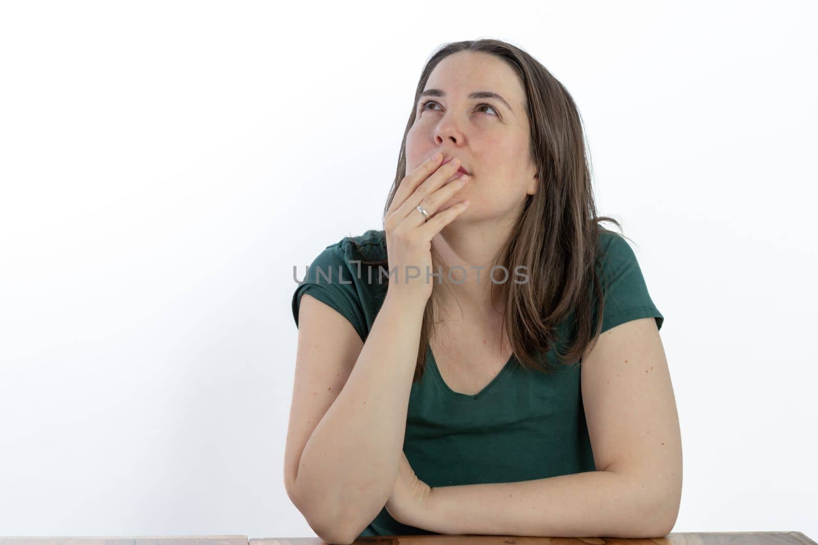 pensive young brunette woman gazing at the sky with her hand on her face white background
