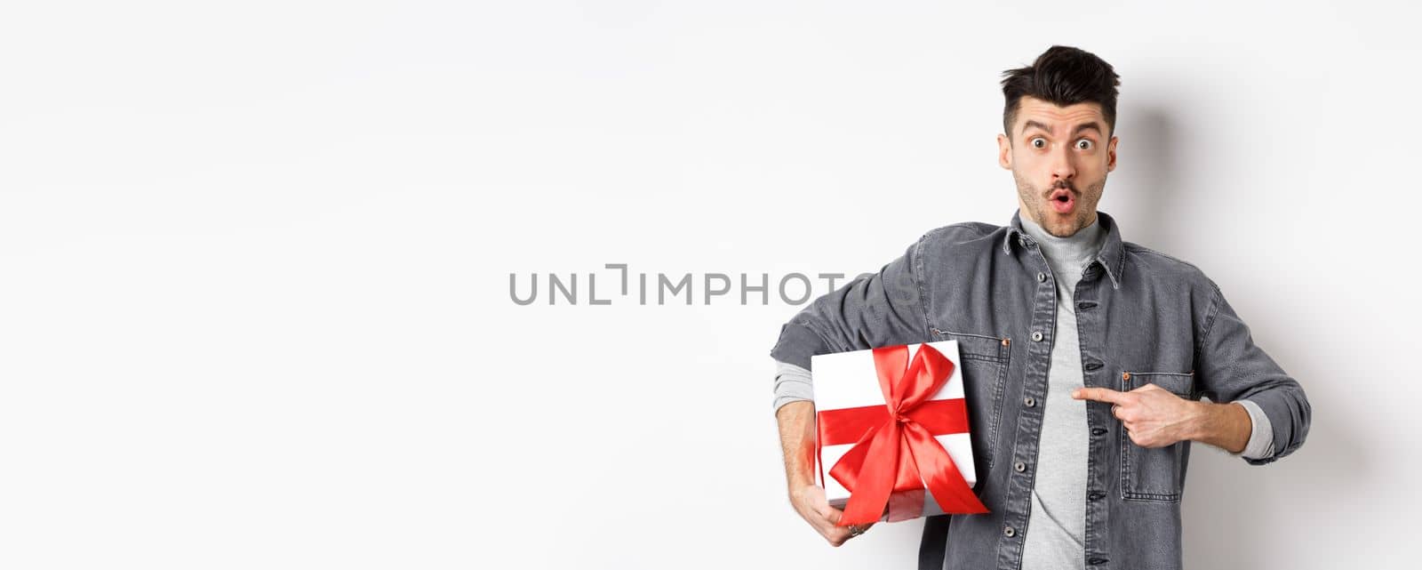 Happy Valentines day. Man shopping for romantic date, pointing at gift box and looking amazed, saying wow impressed, showing lover present, white background.