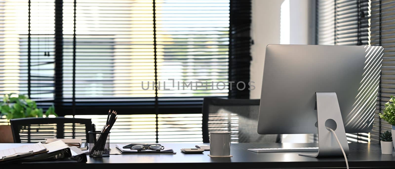 Modern office interior with computer, document supplied and potted plant on blank wooden table.