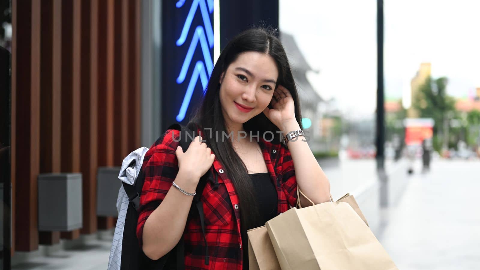 Smiling Asian woman holding her shopping bags and smiling to camera while standing in the city.