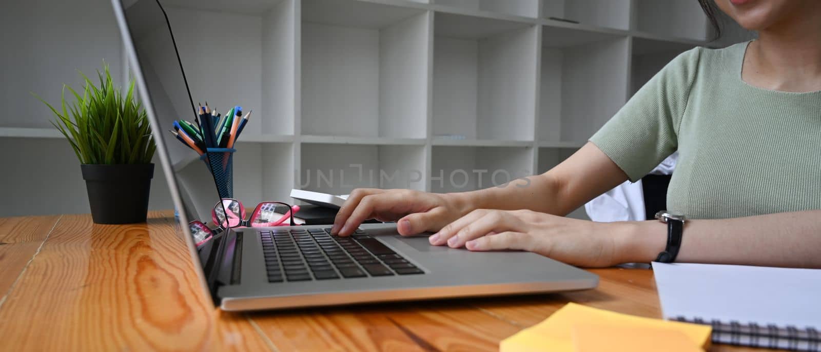 Close up young woman working with laptop computer on wooden desk.