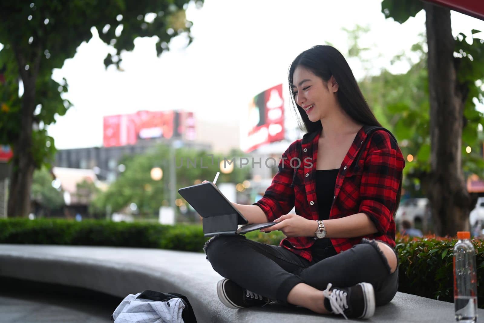Cheerful woman sitting in the city and surfing internet with digital tablet. by prathanchorruangsak