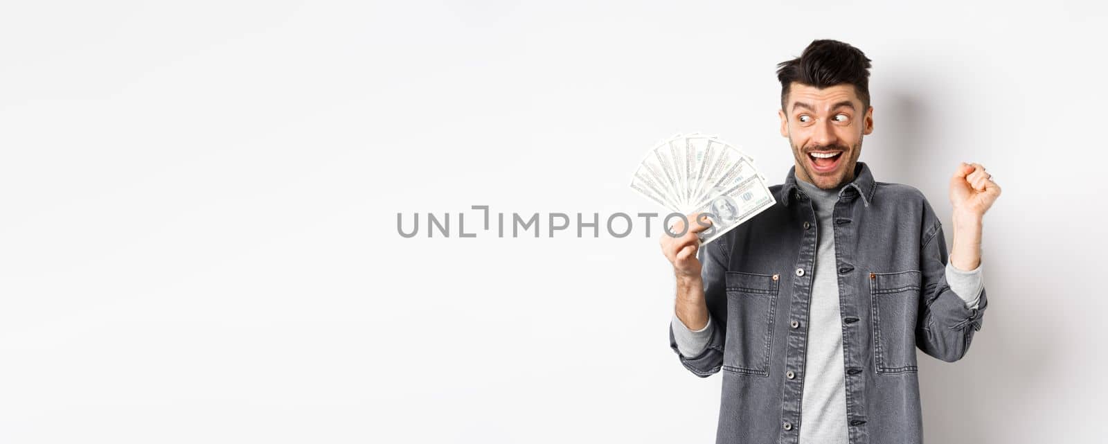 Lucky man winning prize money and scream of excitement, staring at dollar bills happy, standing on white background.