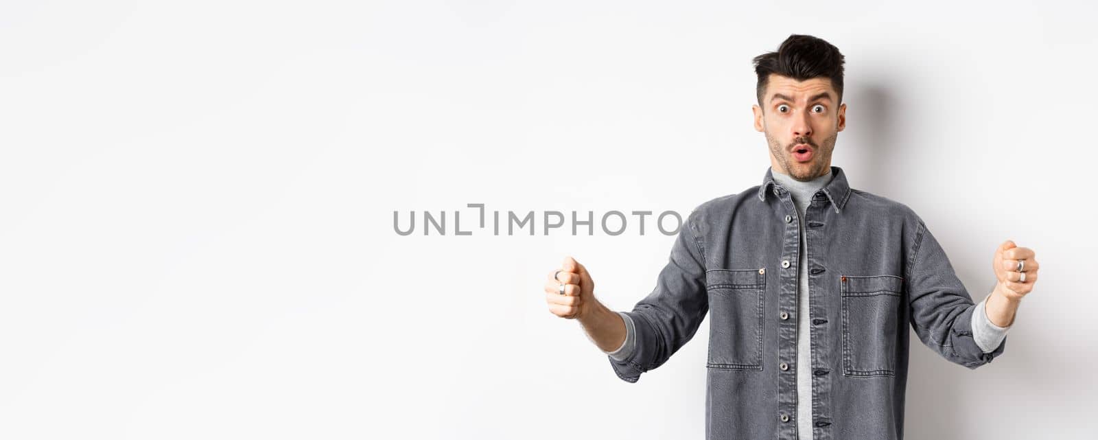 Confused man holding big size object and looking shocked, shaping large thing, standing on white background by Benzoix
