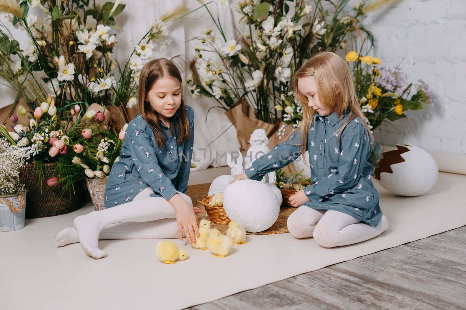 Two girls in a beautiful Easter photo zone with flowers, eggs, chickens and Easter bunnies. Happy Easter holiday. by Annu1tochka