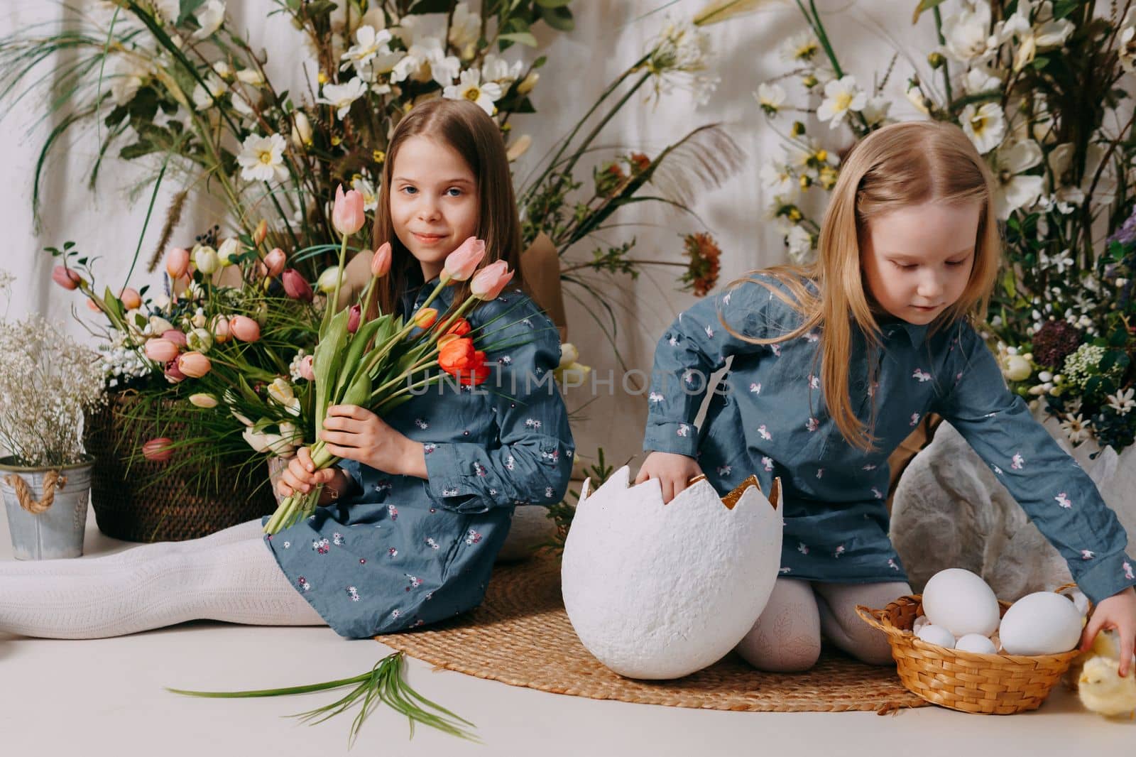 Two girls in a beautiful Easter photo zone with flowers, eggs, chickens and Easter bunnies. Happy Easter holiday. by Annu1tochka