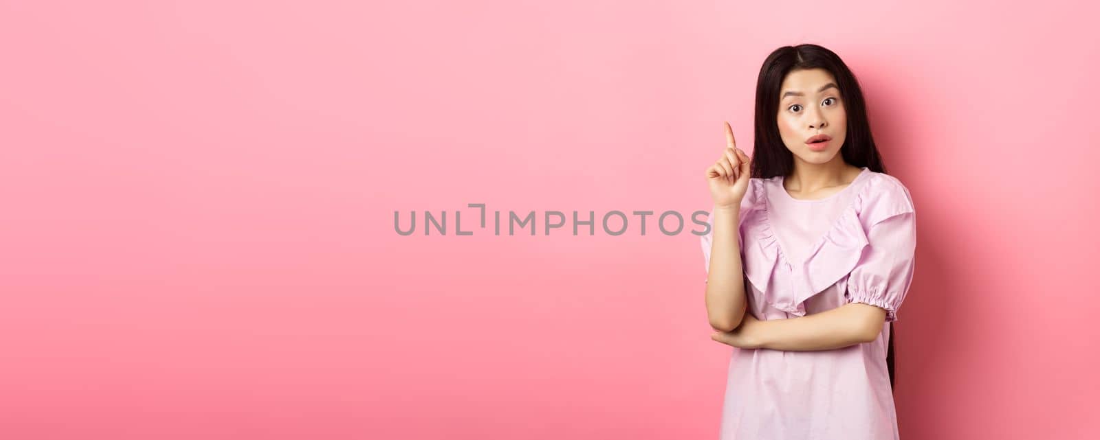 Excited asian woman pitching an idea, raising finger in eureka sign, have plan or solution, standing on pink background.