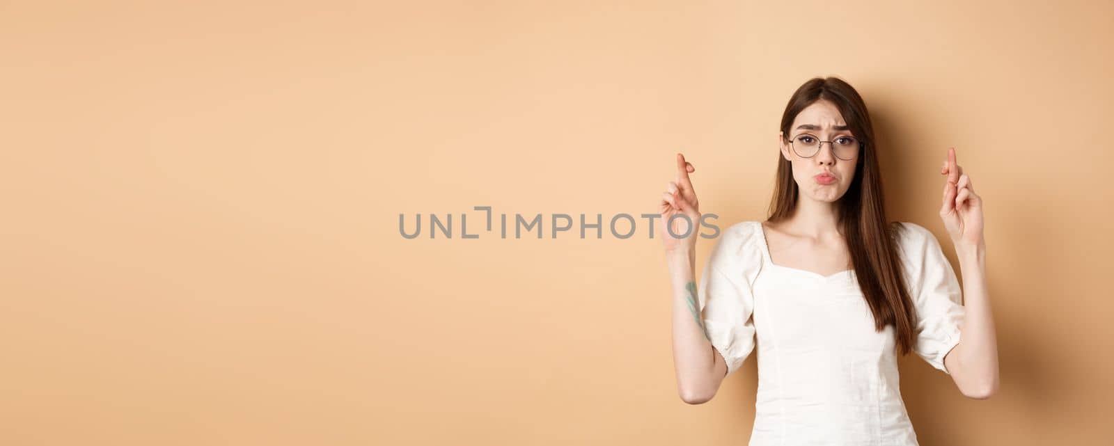 Cute hopeful girl making wish, pucker lips and begging, say please, standing on beige background by Benzoix
