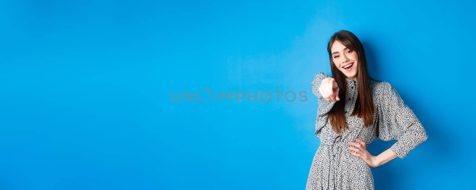 Motivated and excited young woman pointing finger at camera and smiling, congratulating you, praising or inviting, standing happy on blue background by Benzoix