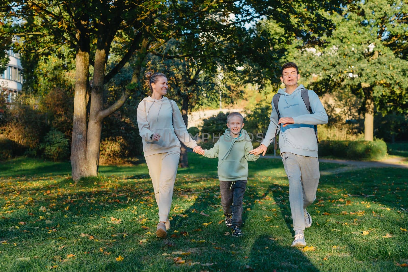 a family mom and 2 sons are having fun, running in the park and jumping. Sons, children, mom, run, play, rejoice, enjoy nature in summer. Family teamwork. Happy family team, running together in field, happily waving their hands. Group of people of different ages. happy family, mom and two sons on an emotional walk. Running and enjoying life in a green field in the park, blue sky, nature by Andrii_Ko