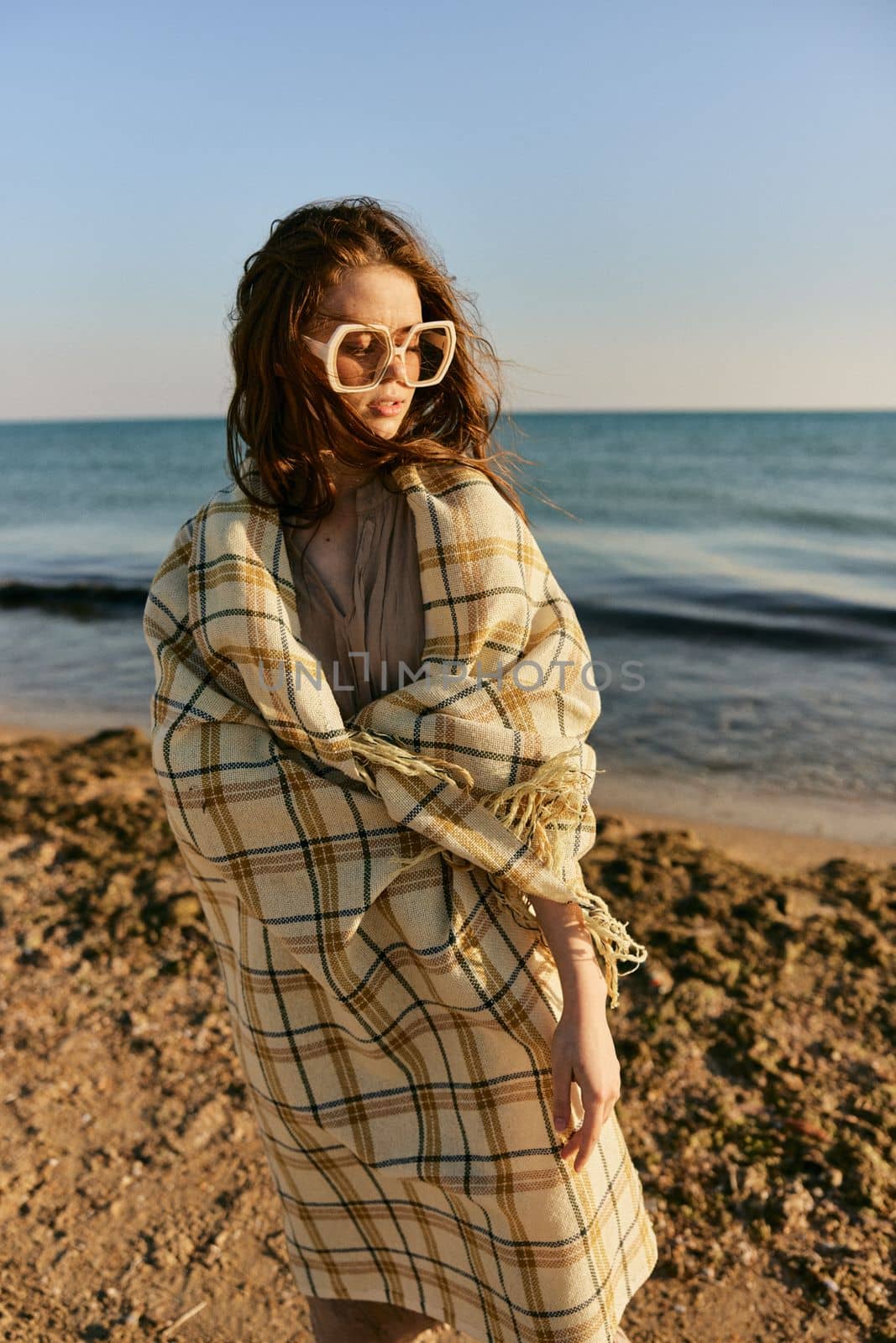 cute woman stands with a plaid during sunset on the beach. Rest, enjoyment. High quality photo