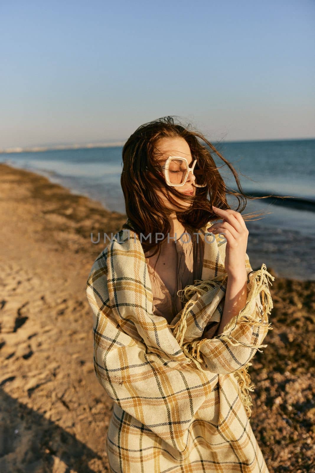 portrait of a woman in a blanket standing on the shore and straightening her hair flying in the wind by Vichizh