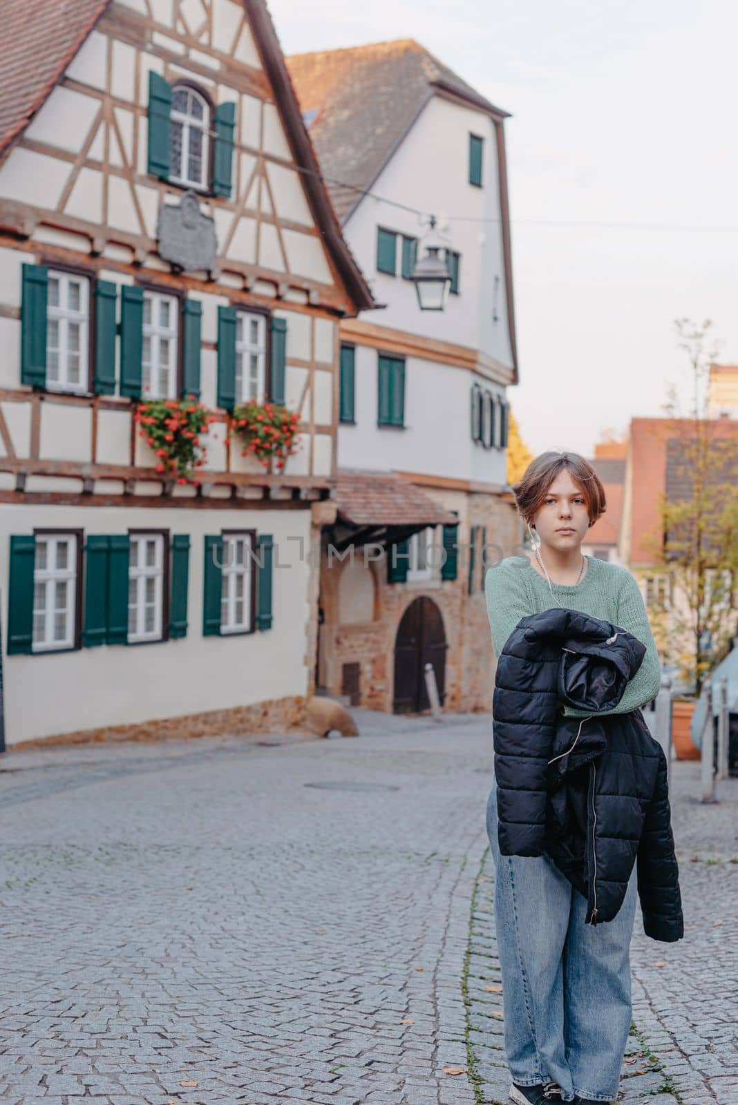 A Beautiful Girl Stands Against The Background Of The Window Of An Old European House. Tourism & Travel Concept. Nice Portrait Of A Young Woman, In Boho Style Outdoors In Fall Autumn Day. Caucasian Female Girl 12 Years Old by Andrii_Ko